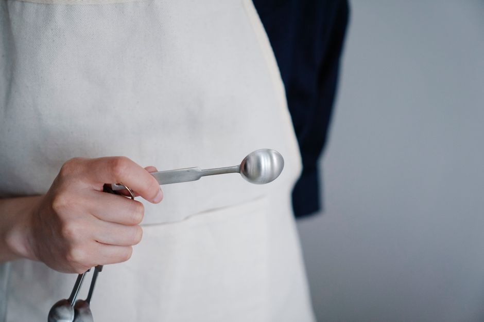 Close-up view of a baker's hand holding a measuring spoon in a kitchen setting.